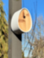 Modern birdhouse with a wooden front attached to a dark post. Clear blue sky and bare trees in the background, conveying a serene mood.